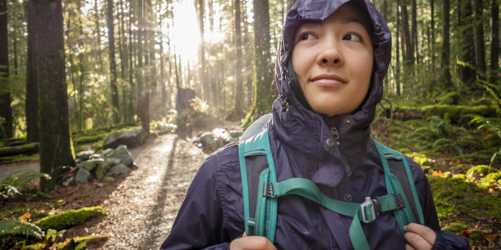 Eurasian Woman Hiking in Rainy Forest, Sunbeams Shining Through Trees