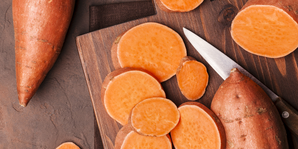Raw sweet potatoes on wooden kitchen board top view. Organic food.