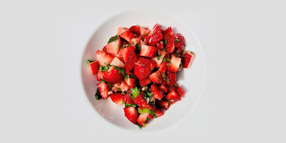 In a bright white bowl, red strawberries are mixed with chopped