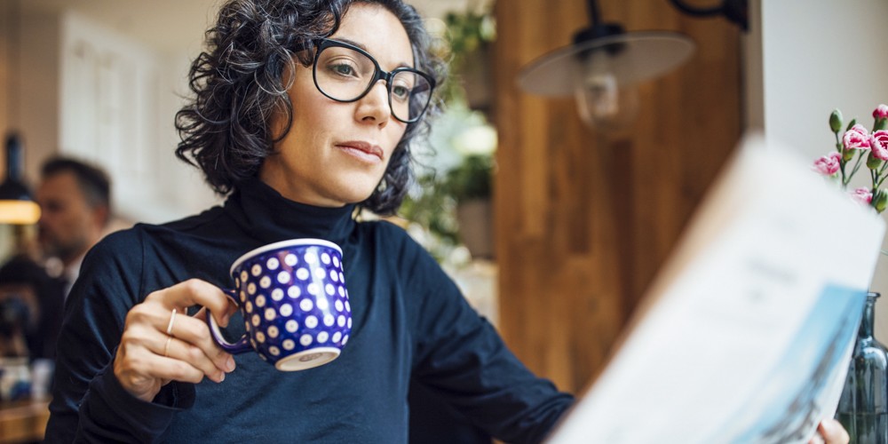 Mid adult businesswoman sitting at cafe reading newspaper and having coffee. Female business professional reading a newspaper in coffee shop. Businesswoman at cafe reading newspaper