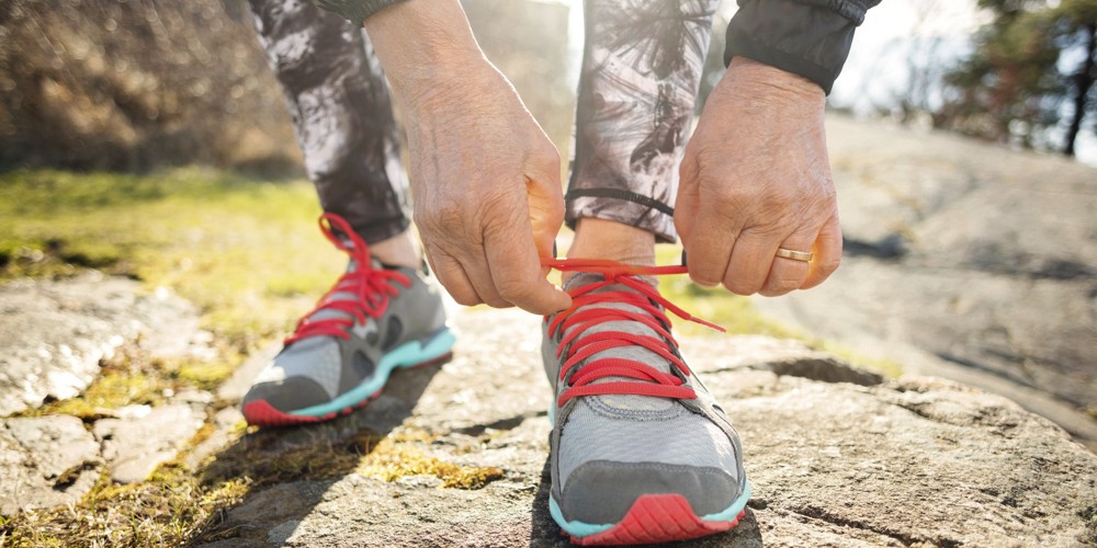 Low section of senior woman tying shoelace while standing on rock